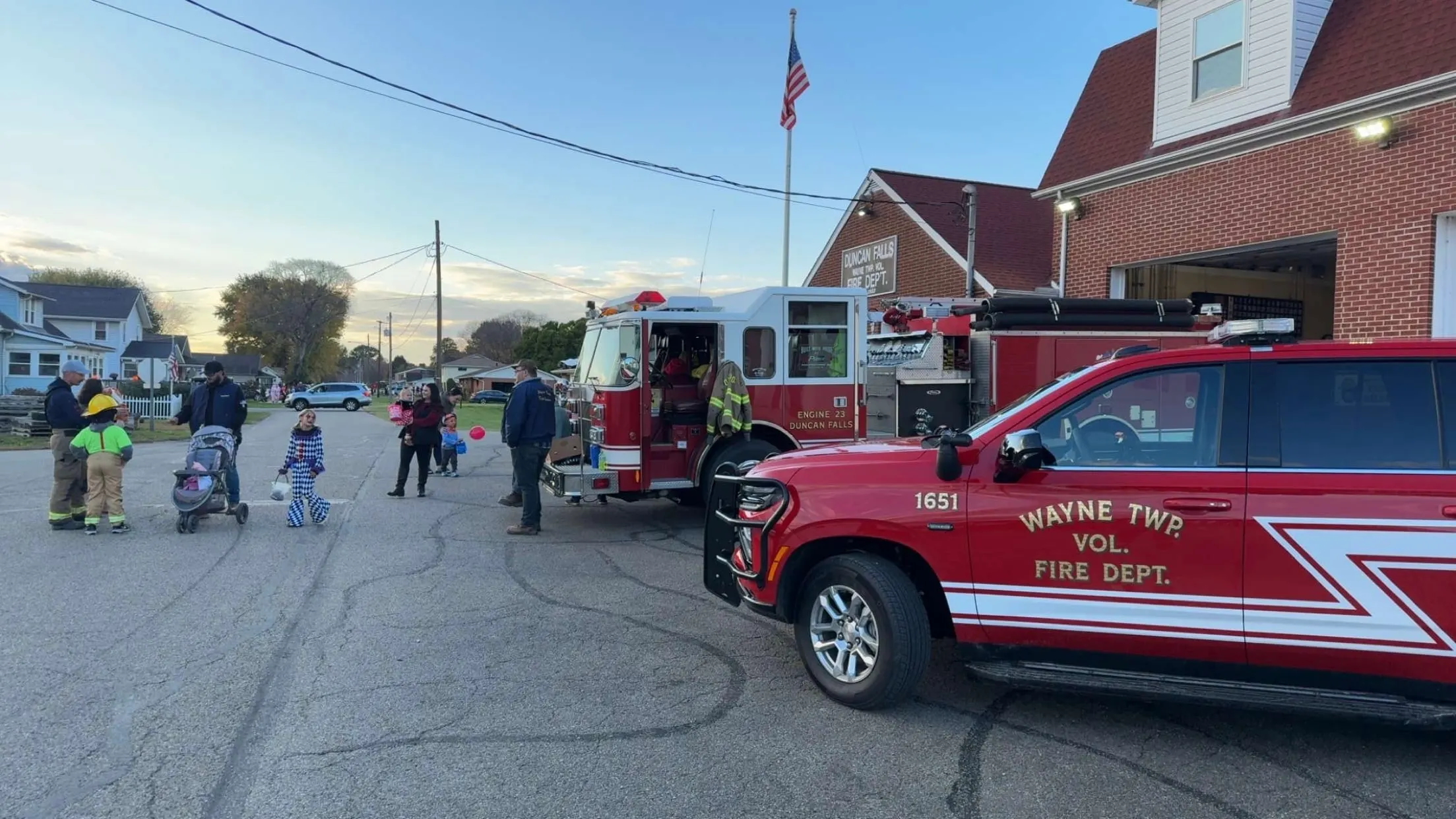 Fire apparatus parked outside a brick building while people gather nearby.