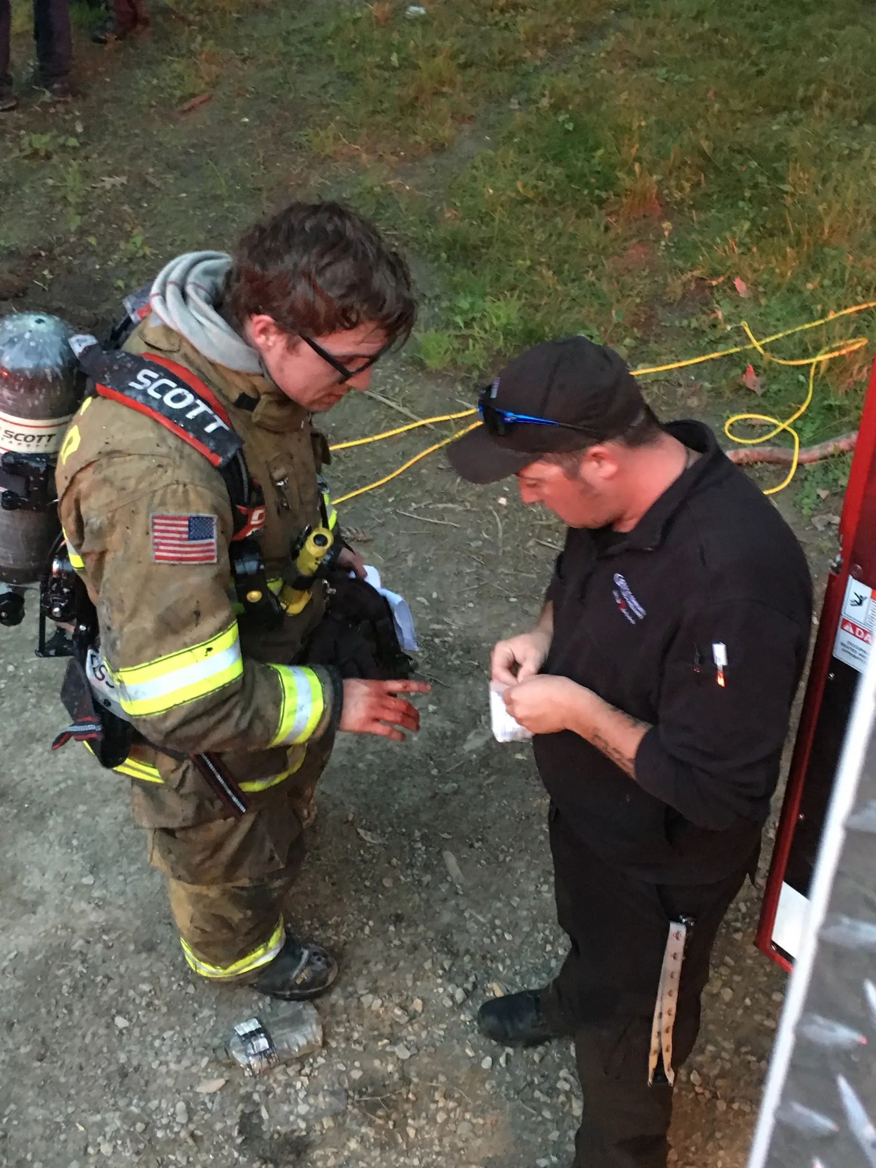 A firefighter and another person checking equipment beside a roadway.