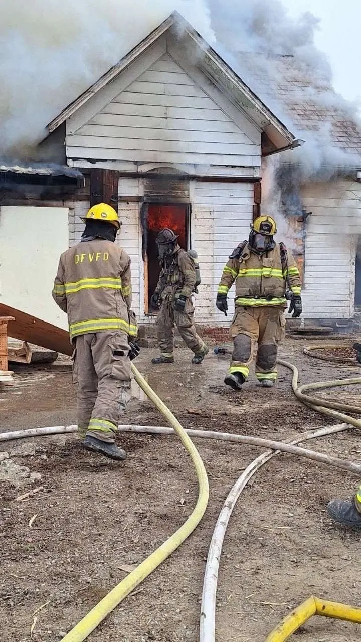 Firefighters advancing a hose line toward a house.