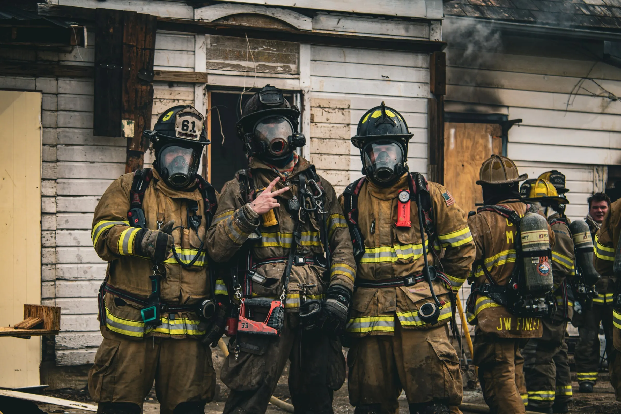 Firefighters in turnout gear standing outside a smoke-stained structure.