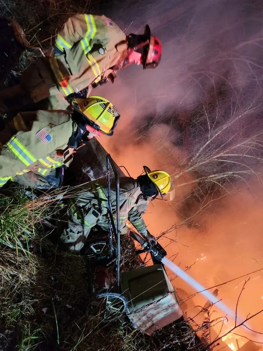Firefighters working near flames and smoke at night.