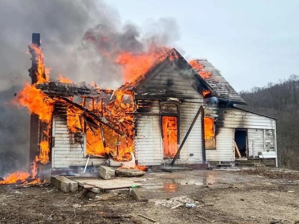 A house with flames through the roof and smoke rising above it.