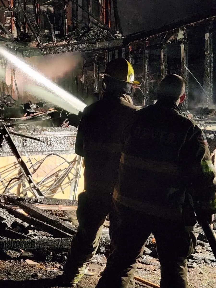 A firefighter directing a hose stream inside a damaged structure.