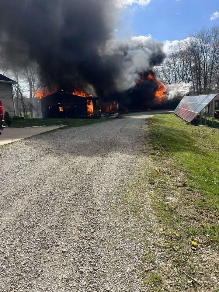 A structure burning near a driveway with smoke rising from the building.