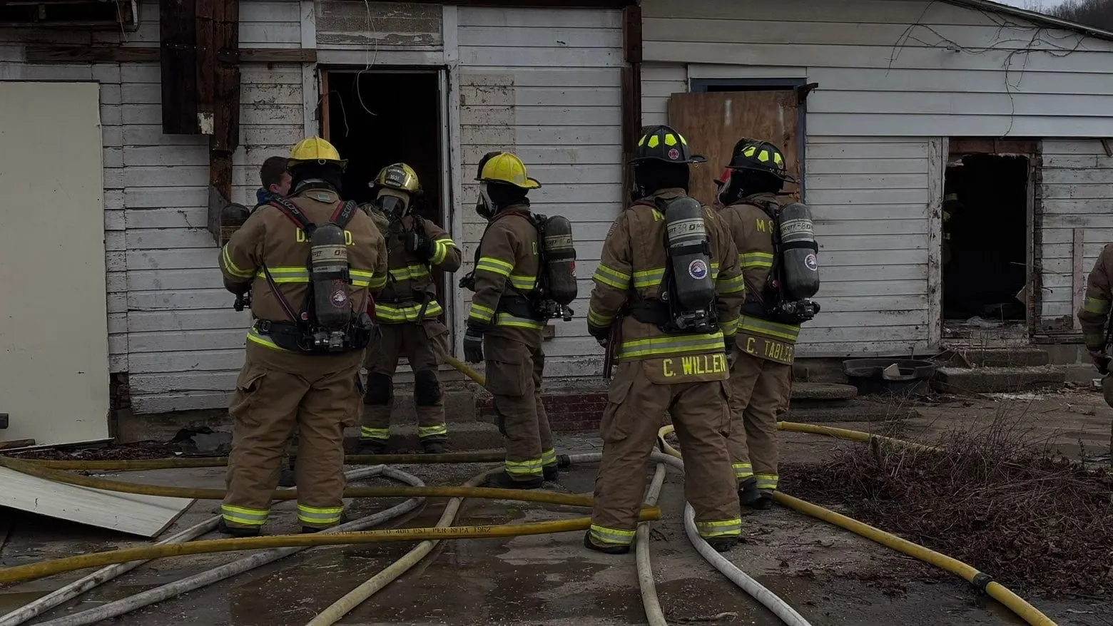 Firefighters in turnout gear working near a smoke-stained house.