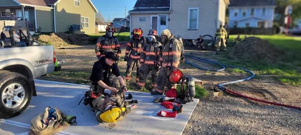 Firefighters standing near turnout gear and hoses during a training scene.