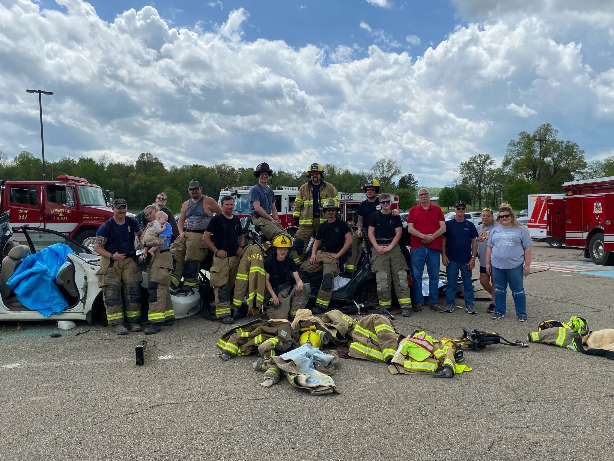 A group of firefighters and trainees gathered with turnout gear in front of apparatus.