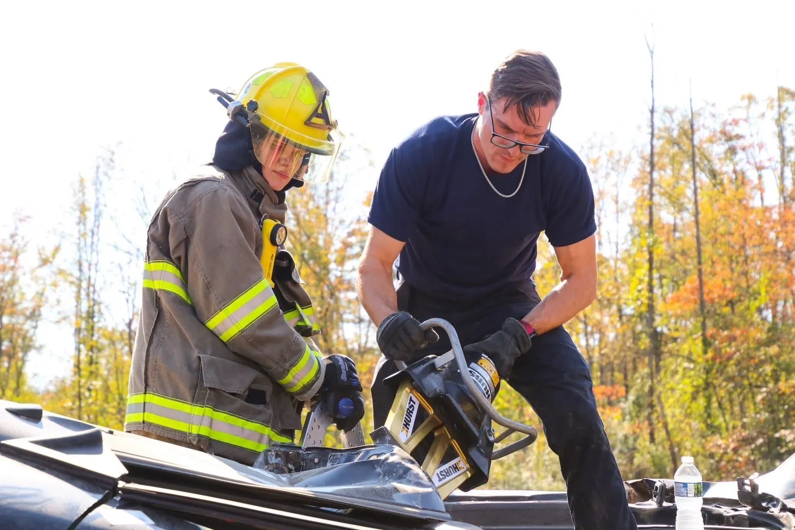 Firefighter and another person working with equipment on a damaged vehicle.